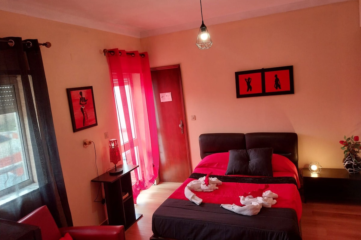 Un dormitorio con cama, mesita de noche, lámpara, ventana con cortinas y puerta.