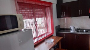 A compact kitchen with a refrigerator, a microwave, a sink, and a table with a chair.