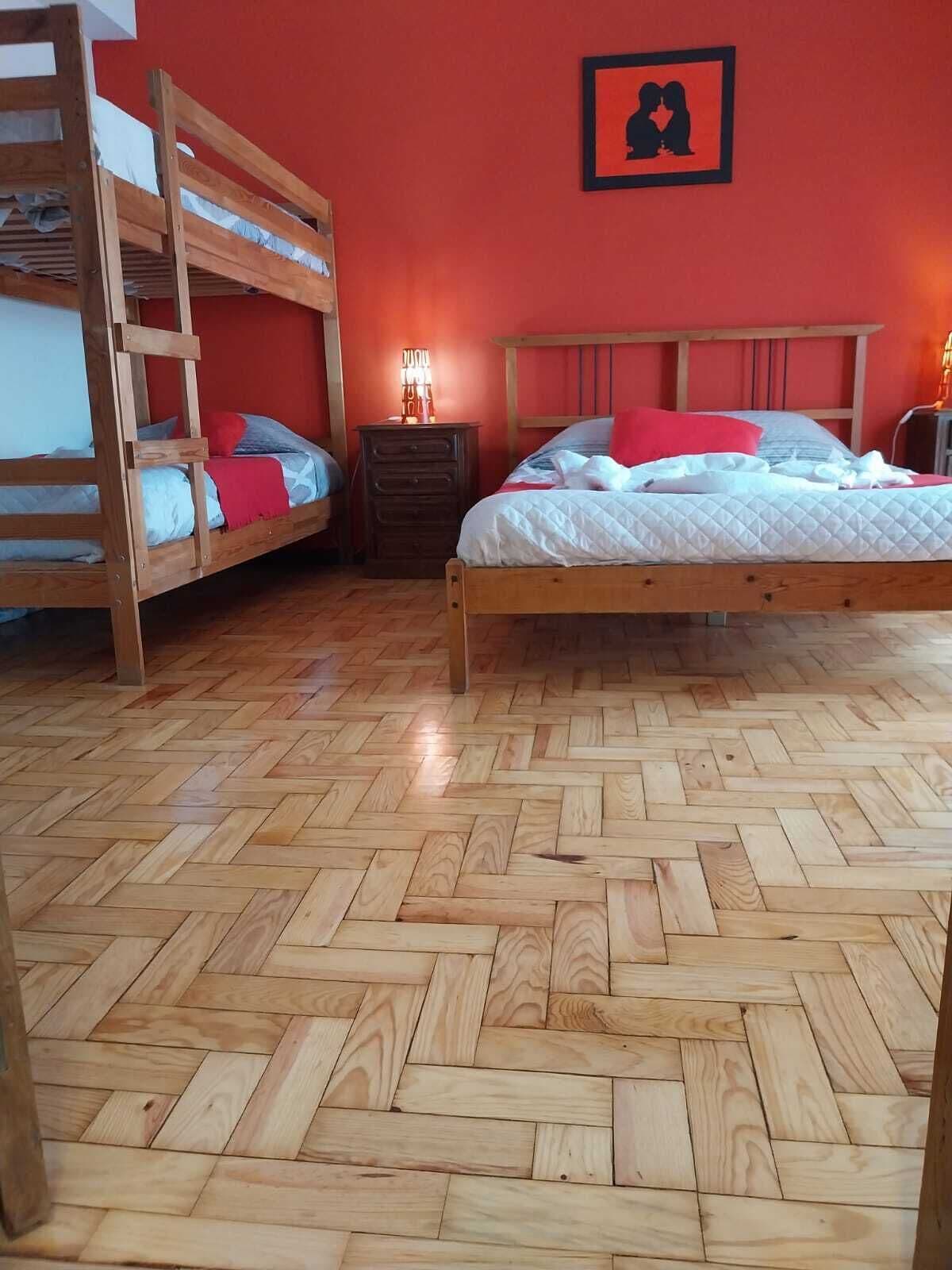 Una habitación con una cama litera de madera, una cama individual, un aparador y un cuadro en la pared.