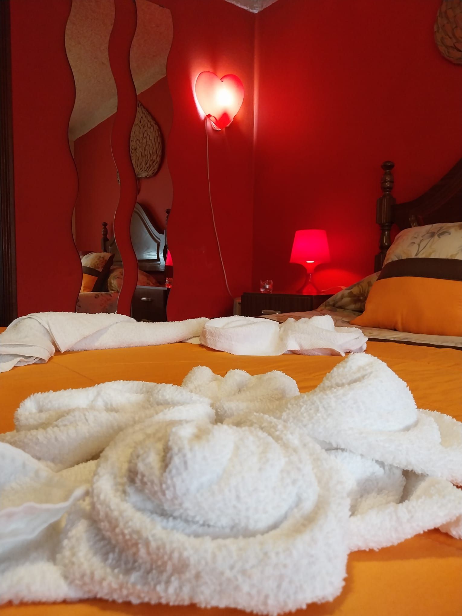 A hotel room with a bed, towels, a heart-shaped light, and a lamp.