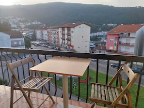 A balcony with a table and two chairs, overlooking a street with buildings and a hilly landscape. - Serra da estrela Superior Seia Huge Flats (Seia)