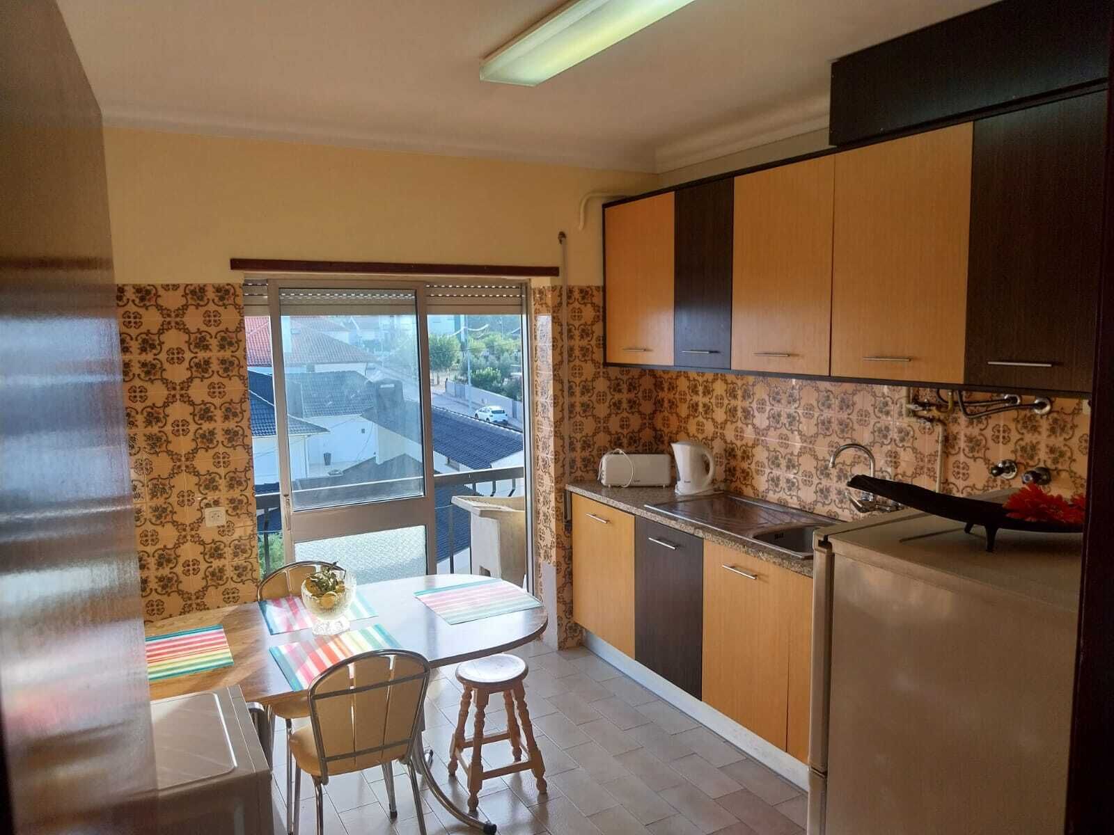 A compact kitchen with a dining area, a refrigerator, a sink, and a window overlooking a street.