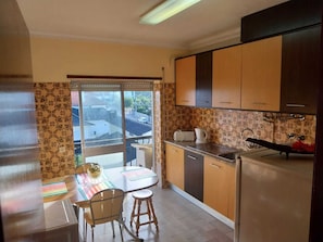 A compact kitchen with a dining area, a refrigerator, a sink, and a window overlooking a street. - Serra da estrela Superior Seia Huge Flats (Seia)