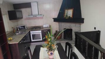 A kitchen with a dining table, chairs, a microwave, an oven, a toaster, a gas stove, a chimney, and a fireplace.