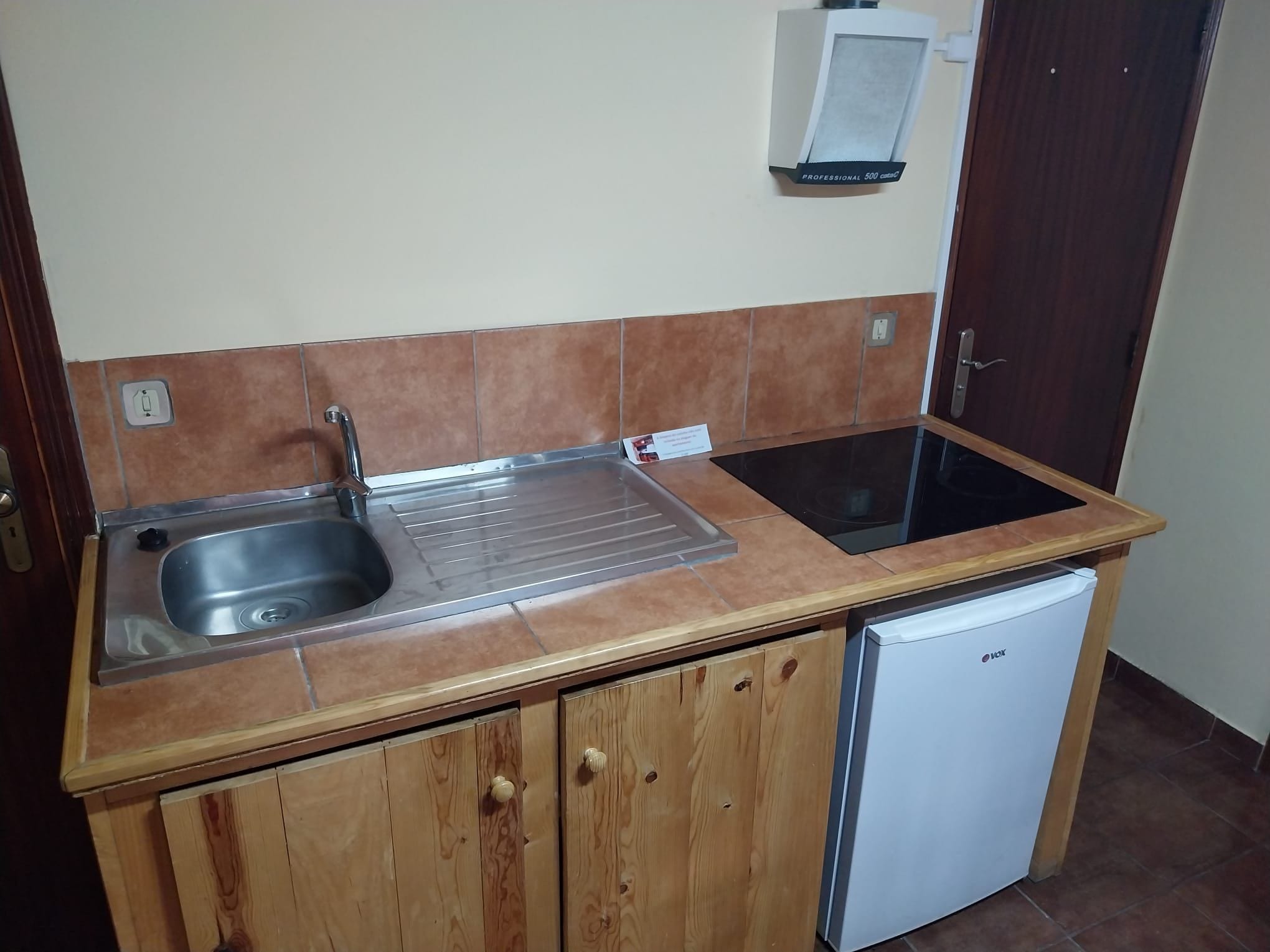 Una cocina compacta con un lavabo, un refrigerador pequeño y un armario.