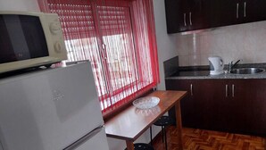 Cocina compacta con refrigerador, microondas, lavamanos y una mesa de madera.