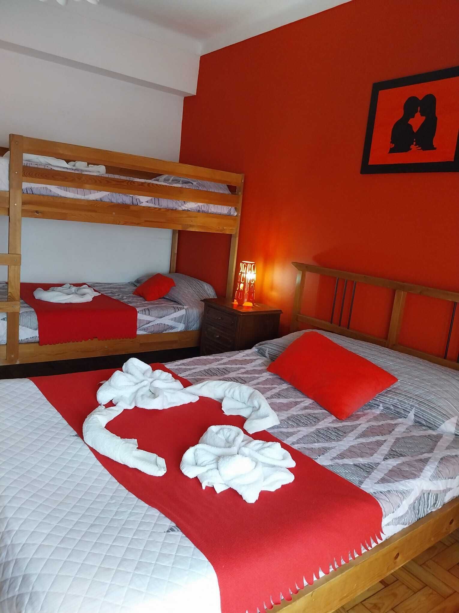 A room with a bunk bed, a single bed with red pillows, and a wall with a framed picture.