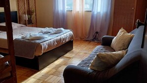A room with a bed, a sofa, a wooden floor, a TV, and a window with curtains.