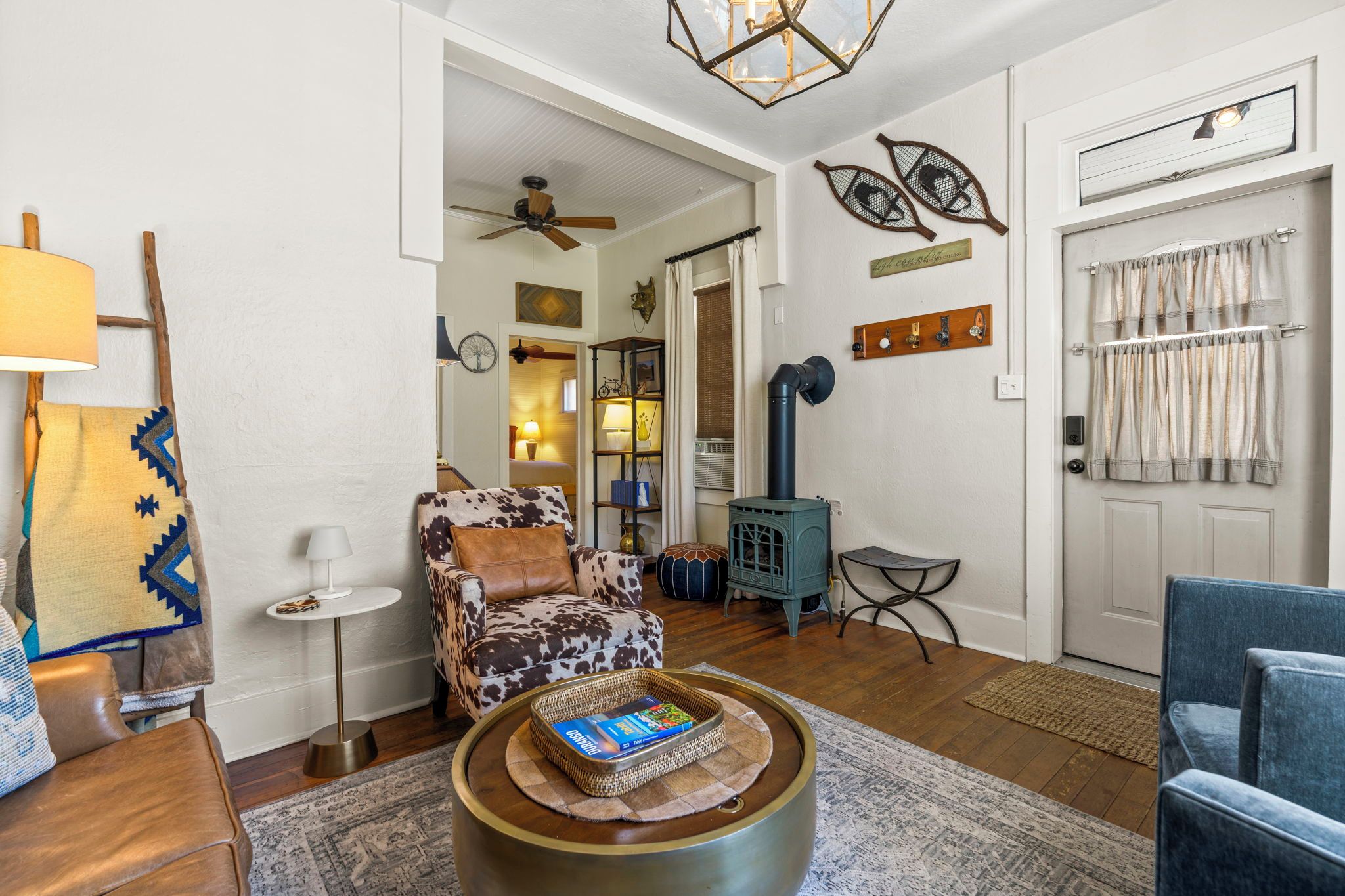 Ein Wohnzimmer mit einem Sofa mit Kuhmuster, einem Couchtisch mit einem Buch, einem blauen Sessel, einem Kamin und einem Deckenventilator.