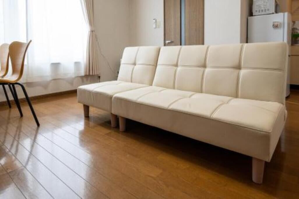 A modern living room with a white sofa, a wooden floor, and a window with curtains.