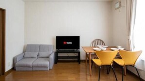 Un salon comprenant un canapé, un téléviseur, une table à manger avec des chaises et une fenêtre avec des rideaux.