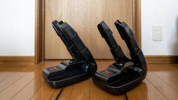Two upright vacuum cleaners on a wooden floor with a wooden door and a white wall in the background.