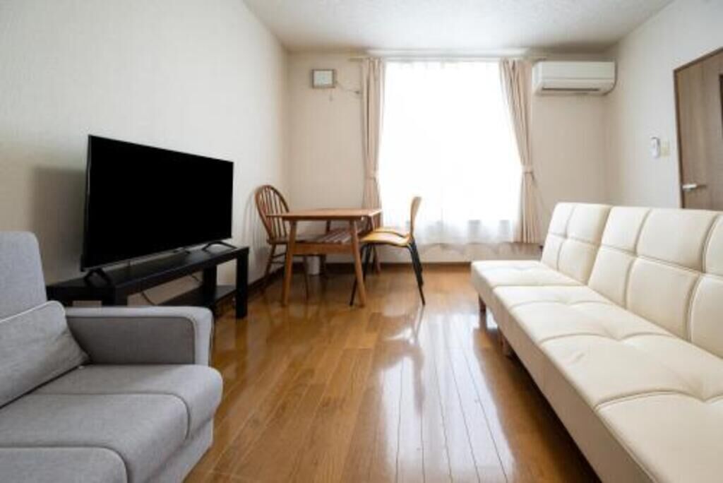 Una habitación con sofá, televisor, mesa de comedor con sillas y ventana con cortinas.