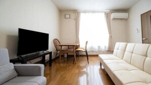 Une pièce comprenant un canapé, un téléviseur, une table à manger avec des chaises et une fenêtre avec des rideaux.