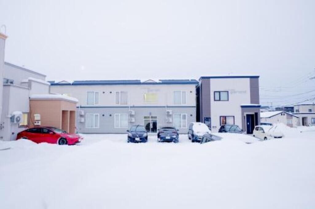 Un edificio con varios espacios de estacionamiento, un auto rojo y el suelo cubierto de nieve.