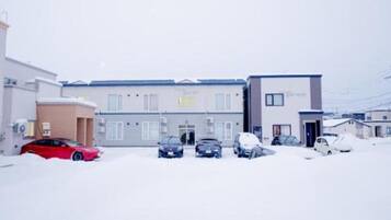 Un edificio con varios espacios de estacionamiento, un auto rojo y el suelo cubierto de nieve.