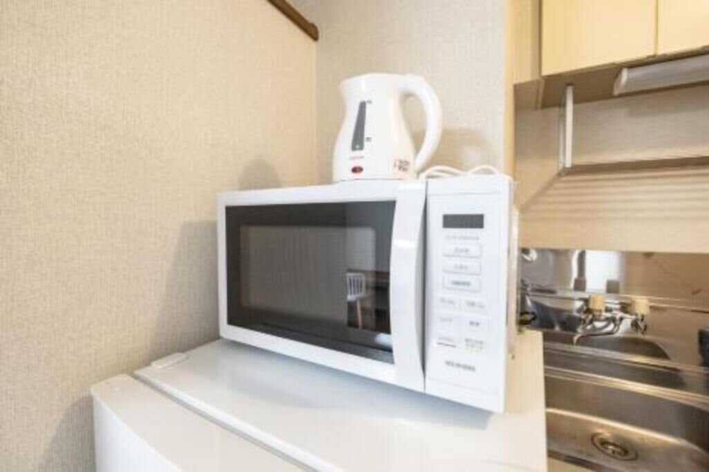 Een witte magnetron op een wit aanrecht, met een roestvrijstalen spoelbak en kasten op de achtergrond.