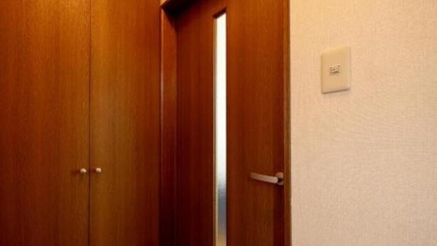 Une porte en bois avec une petite fenêtre, une poignée de porte et un interrupteur sur le mur.