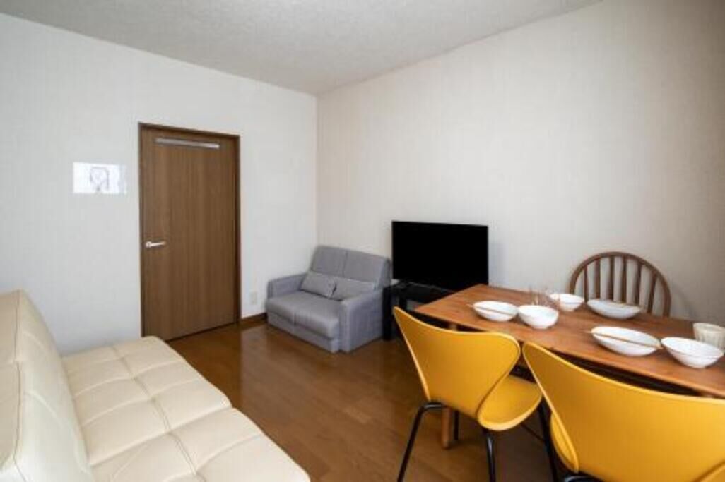 Una habitación con sofá, una mesa de comedor con sillas, televisión y una puerta.