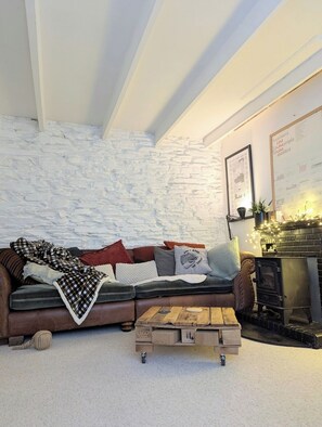 Ein gemütliches Wohnzimmer mit Steinwand, braunem Ledersofa, Couchtisch aus Holz und Kamin.