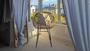 Une pièce dotée d’une grande fenêtre, d’un fauteuil en osier et de rideaux légers.
