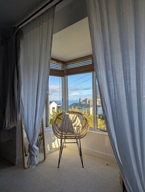 Ein Zimmer mit großem Fenster, Korbsessel und transparenten Vorhängen.