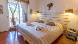 Un dormitorio con cama, cortinas, cabecera, mesita de noche y velador.
