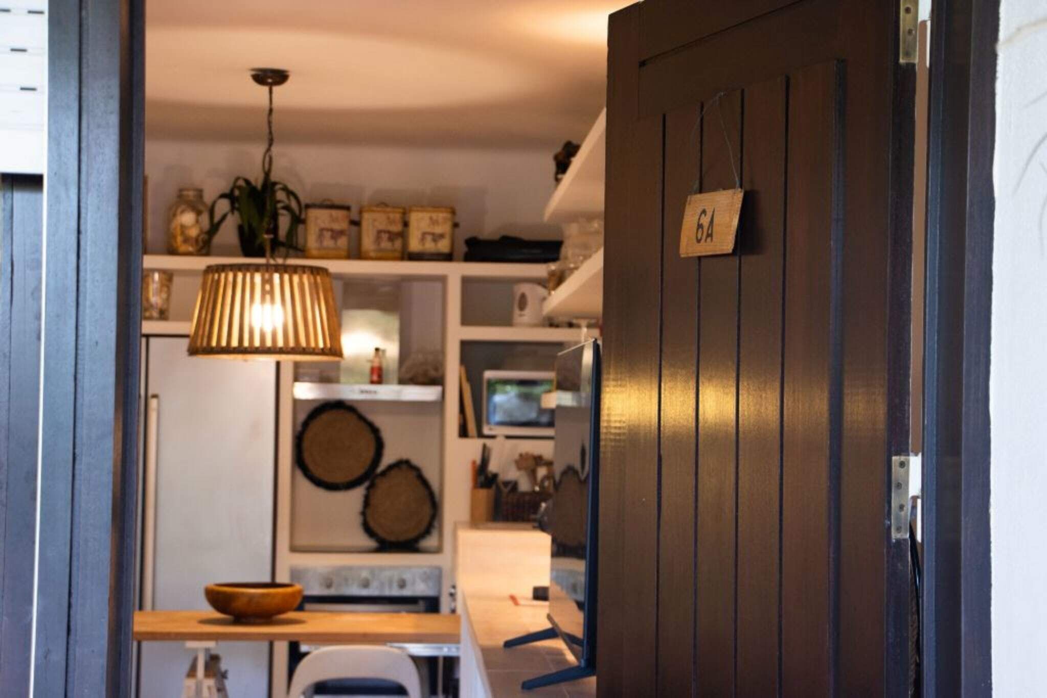 A kitchen with a wooden door, a hanging light fixture, and shelves with various items.