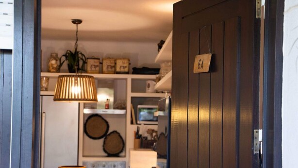 Una cocina con puerta de madera, lámpara colgante y repisas con varios objetos.