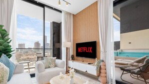 Een moderne woonkamer met een grote televisie, een bank, een salontafel en uitzicht op een stadsgezicht.