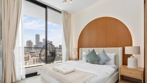 Een moderne hotelkamer met een groot bed, stadszicht, een houten hoofdbord en nachtkastje met lamp.