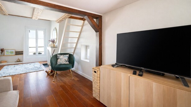 A living room with a large flat-screen TV on a wooden cabinet, a green armchair, a wooden floor, and a staircase leading to an upper level. - Appartement Panorama Sacré-Cœur - Welkeys (Paris)