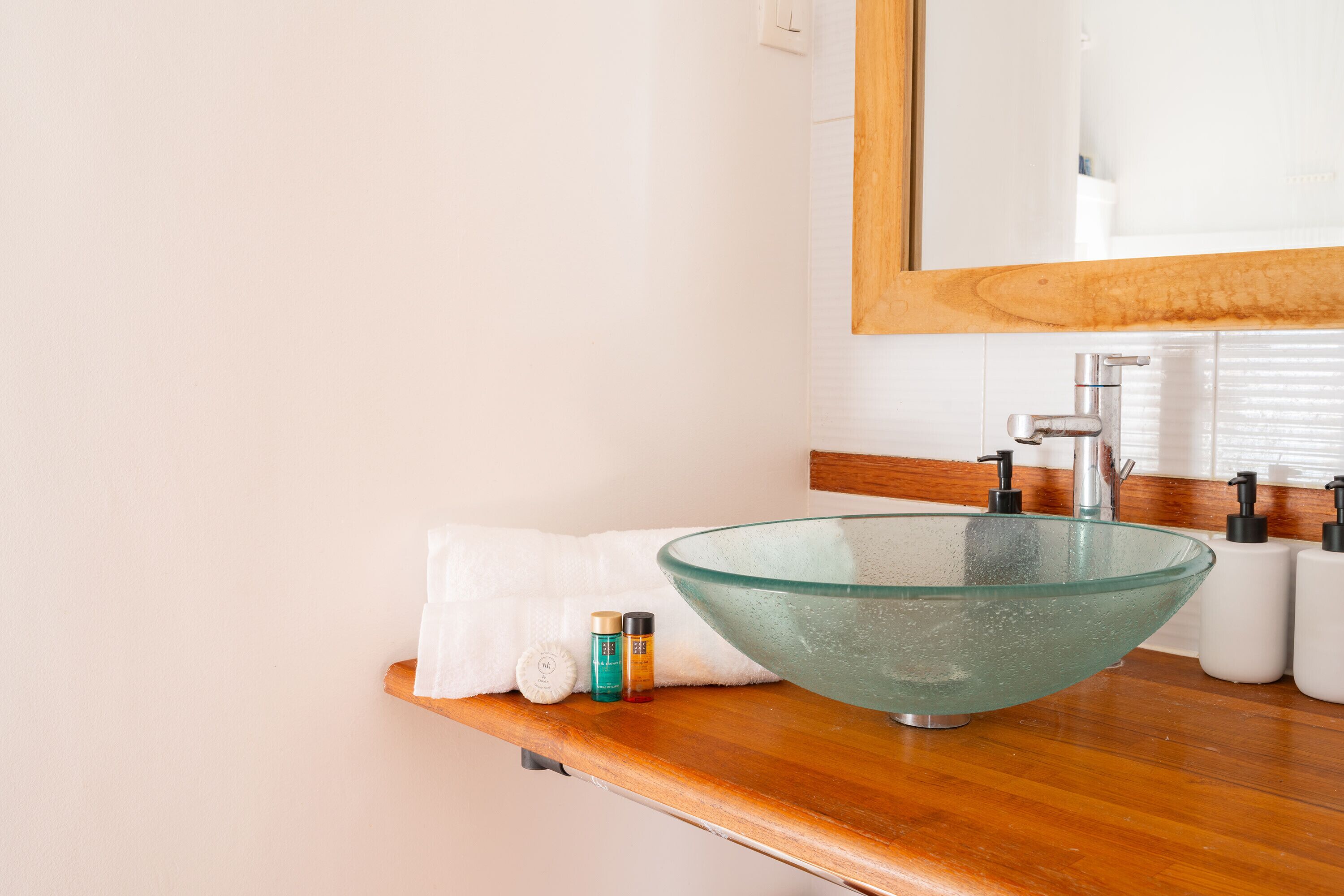 A modern bathroom with a glass bowl sink, wooden countertop, and a mirror above.