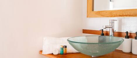 A modern bathroom with a glass bowl sink, wooden countertop, and a mirror above.