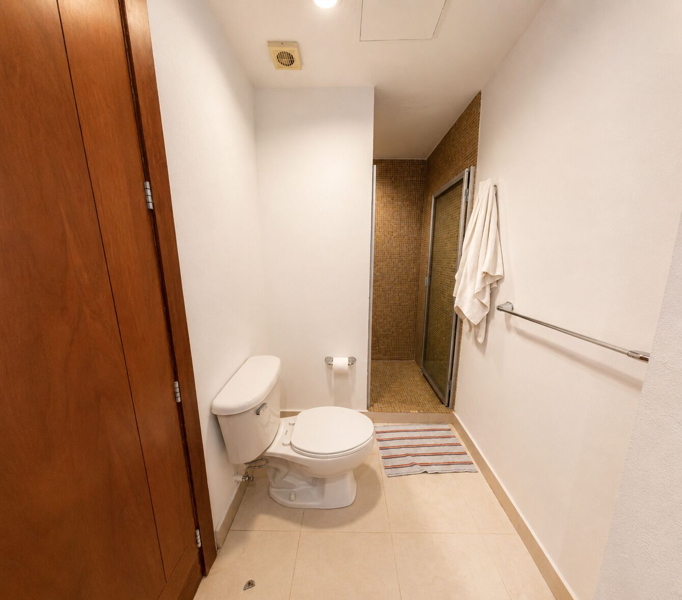 Un baño pequeño con inodoro, zona de ducha y perchero para toallas.