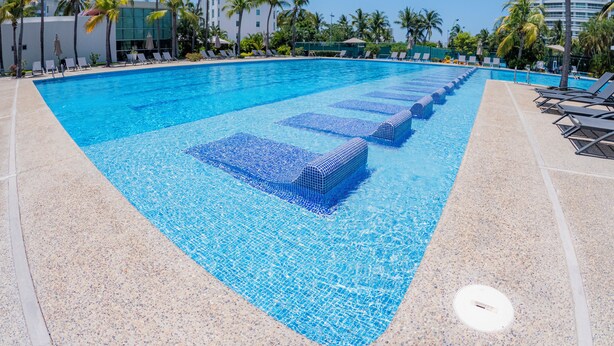 A swimming pool with clear blue water, surrounded by lounge chairs and palm trees.