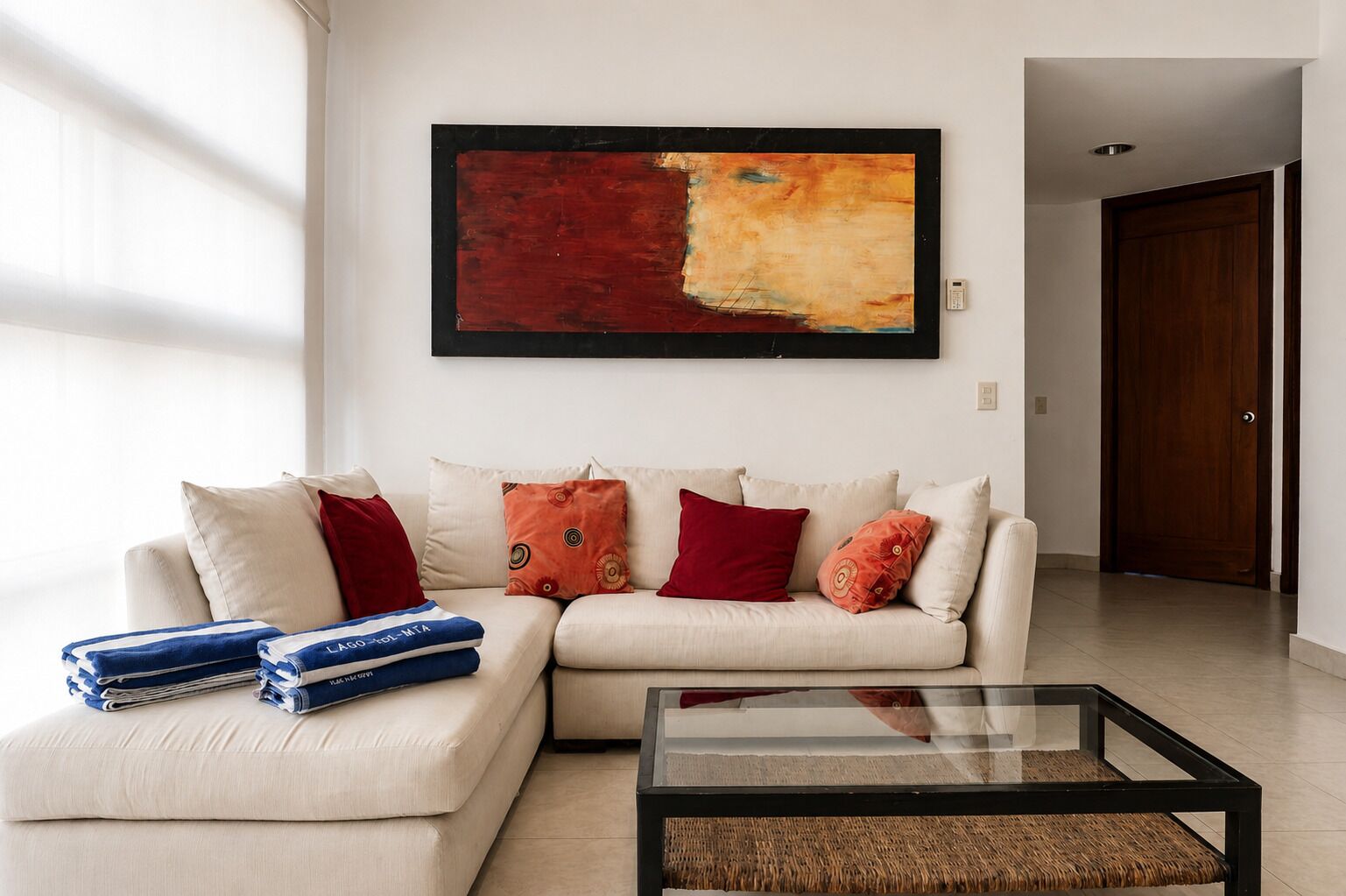 A living room with a sectional sofa, a glass coffee table, and a large abstract painting on the wall.