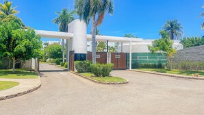 A gated entrance with a modern building, palm trees, and a clear sky.
