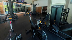 A gym with various exercise equipment, a large mirror, and a television screen.