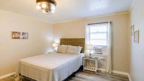 Een slaapkamer met een bed, nachtkastje, lamp en een raam met gordijnen.