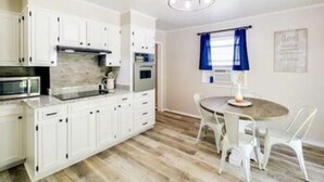 Een moderne keuken met witte kasten, een magnetron en een eethoek met een ronde tafel en witte stoelen.
