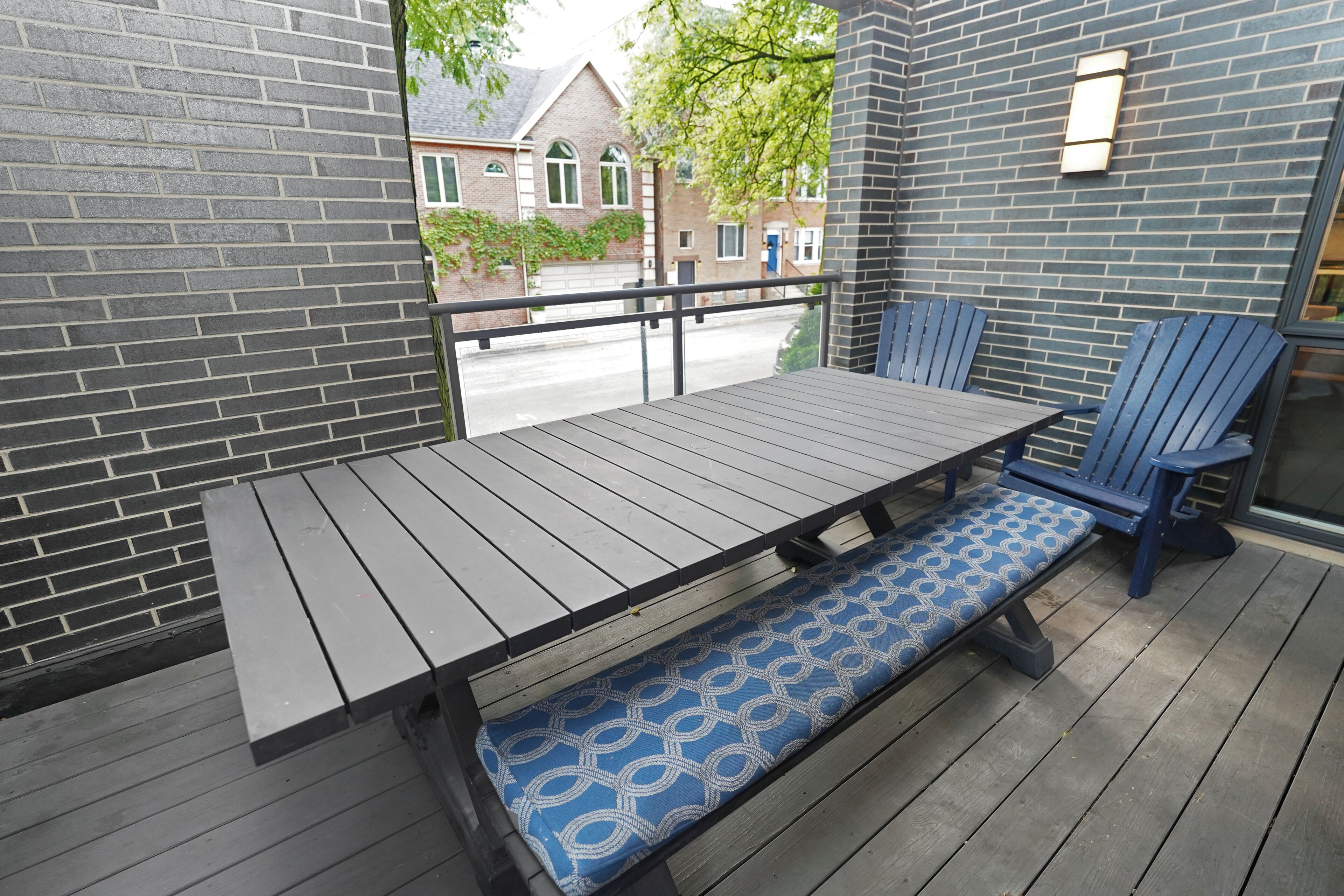 Een houten terras met een tafel, stoelen, een bankje en een uitzicht op gebouwen door een raam.