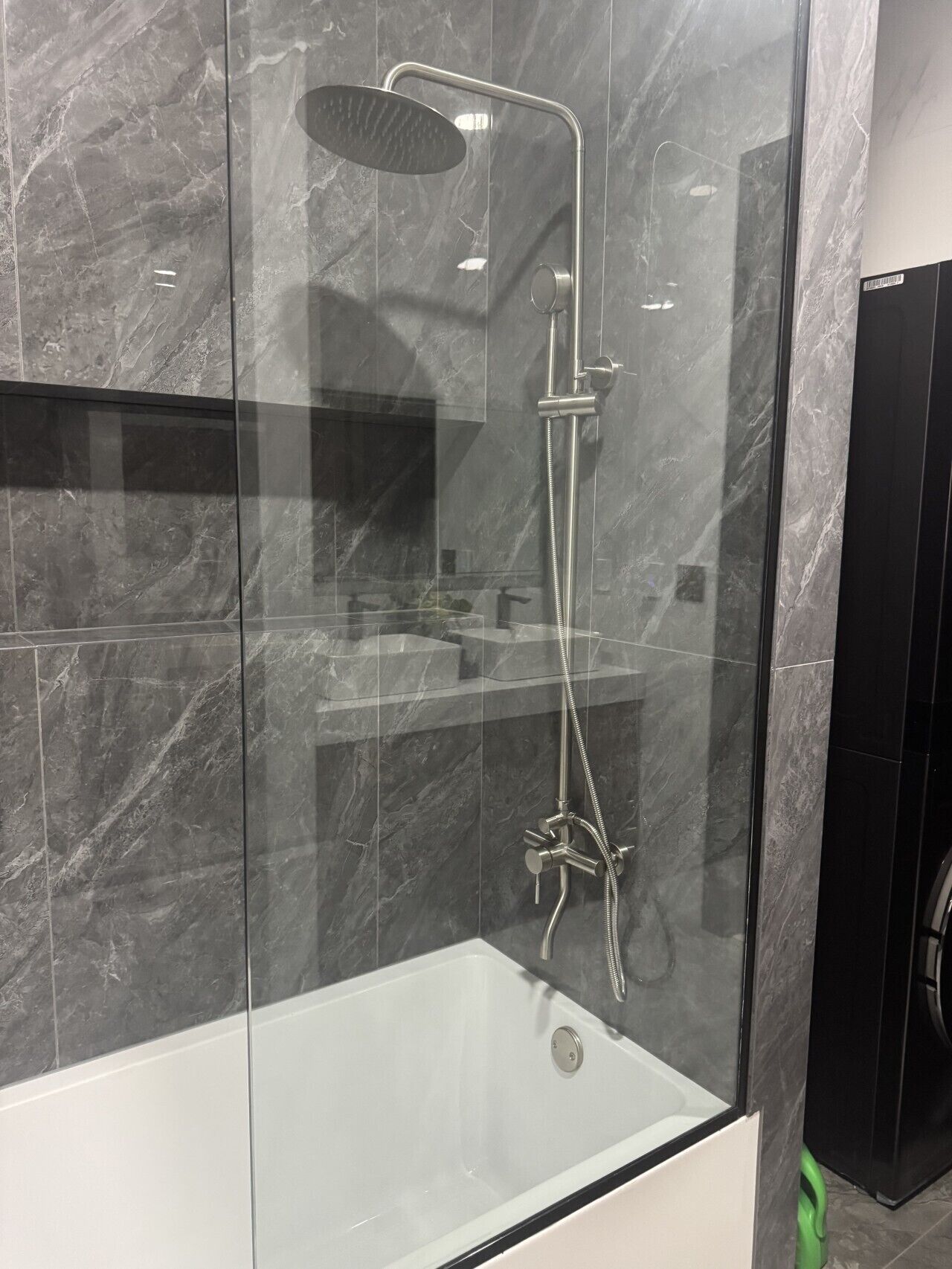 Een moderne badkamer met een douche in een glazen cabine, een witte badkuip en marmeren wanden.