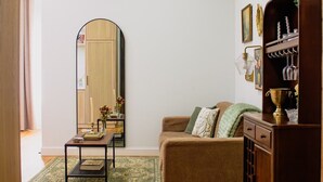 A living room with a wooden floor, a brown sofa, a coffee table, a mirror, and a wooden cabinet with a trophy.