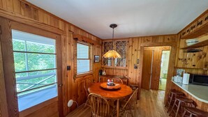 Ein Holzinterieur mit Esstisch, Stühlen, einer Küchenzeile und Blick durch ein Fenster.