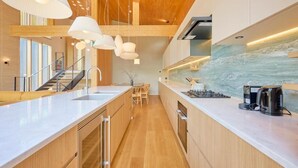 A modern kitchen with wooden cabinetry, a marble backsplash, and pendant lighting. - Grand Tsuru B (Niseko)
