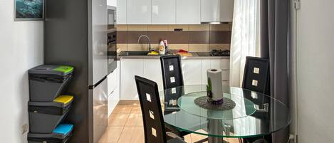 A compact kitchen with white cabinets, a glass-top dining table, and black chairs.