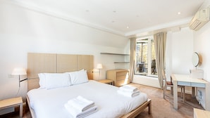 A hotel room with a bed, bedside tables, a desk, a chair, and a window with curtains. - Penthouse With Terrace on Maida Vale Border (London)
