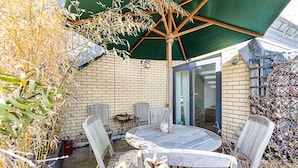 A patio with a round table and chairs, a green umbrella, and a brick wall. - Penthouse With Terrace on Maida Vale Border (London)
