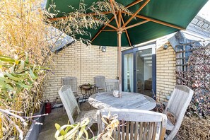 Eine Terrasse mit einem runden Tisch und Stühlen, einem grünen Sonnenschirm und einer Ziegelwand.